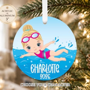 May include: A round ornament featuring a cartoon illustration of a blonde swimmer in a pink swimsuit and pink goggles, swimming in blue water with splashes. The name CHARLOTTE and the year 2026 are printed in white text. Includes a white ribbon.