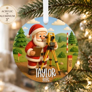 May include: A round Christmas ornament featuring a cartoon Santa Claus using a yellow surveying total station on a tripod. Santa holds a clipboard in a grassy field with pine trees and a survey marker labeled Survey Point 12. Text reads Taylor 2026.