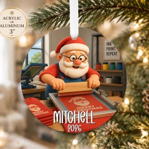 May include: A round 3-inch acrylic or aluminum ornament featuring a cartoon Santa Claus wearing glasses and blue overalls, screen printing a red shirt with the text Merry Christmas. The ornament includes the custom name Mitchell and the year 2026.