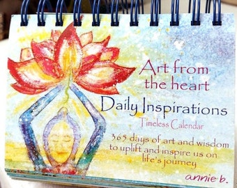 May include: A colorful calendar with a watercolor painting of a person holding a lotus flower. The text on the cover reads "Art from the heart Daily Inspirations Timeless Calendar 365 days of art and wisdom to uplift and inspire us on life's journey annie b."