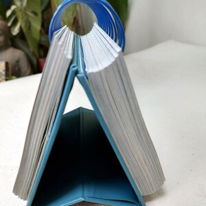 May include: A teal blue desktop calendar with a blue spiral binding. The calendar is closed and standing upright on a white surface.