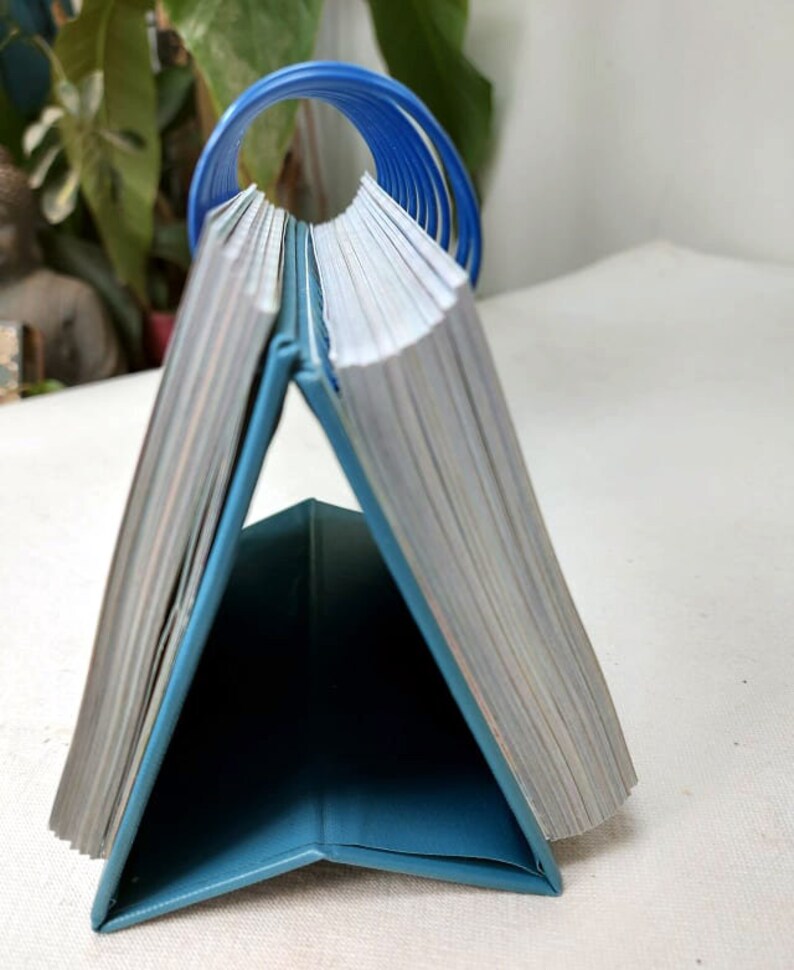 May include: A teal blue desktop calendar with a blue spiral binding. The calendar is closed and standing upright on a white surface.