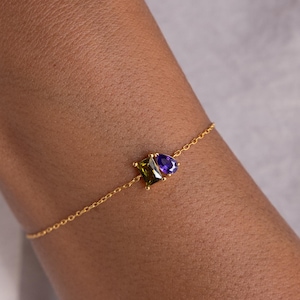 May include: A gold chain bracelet with a purple and green gemstone pendant.