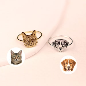 This image features 2 of our pet photo rings,  one with a custom portrait of a cat engraved onto the face of an 18K gold ring and an image of a dog engraved on a Silver ring. The rings are shown in a close-up photo against a plain white background.