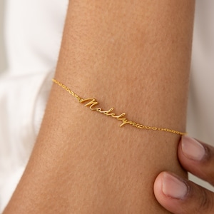 May include: A gold chain bracelet with the name "Madelyn" written in cursive script.