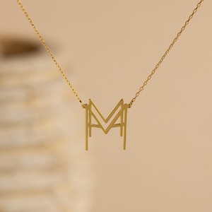 May include: A gold chain necklace with a geometric letter M pendant.