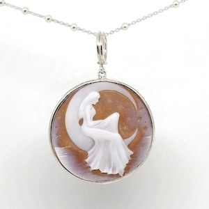 May include: A silver chain necklace with a cameo pendant featuring a white woman sitting on a crescent moon with stars in the background.