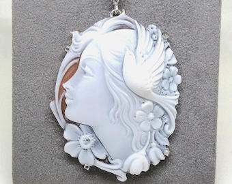 May include: A white cameo pendant necklace featuring a woman's profile with a dove and floral details. The pendant is set on a silver chain.