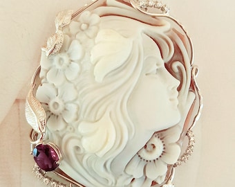 Può includere: Un ciondolo in cammeo bianco con il profilo di una donna con intricati dettagli floreali. Il ciondolo è incastonato in argento con un accento di pietra preziosa viola.