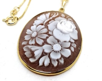 May include: A gold chain necklace with a cameo pendant featuring a carved floral design. The cameo is oval-shaped and has a brown background with white flowers.