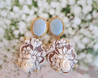 May include: A pair of gold tone earrings with a light blue oval shaped stone and a white carved floral design.