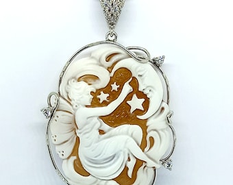 Pode incluir: Um colar de corrente de prata com um pingente de camafeu que apresenta uma figura esculpida em branco de uma mulher segurando uma estrela. O camafeu está engastado em uma moldura de prata com um design em espiral e acentuado com pequenas pedras transparentes.