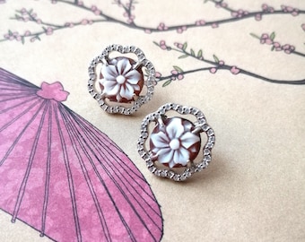 May include: A pair of silver earrings with a white flower design set in a brown cameo. The earrings have a delicate, intricate design.