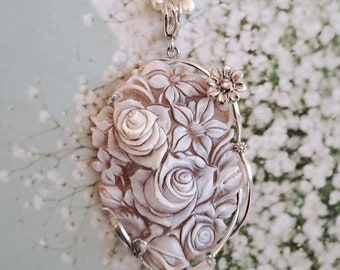 May include: A delicate silver necklace with a carved white shell pendant featuring a cluster of roses and other flowers. The pendant is surrounded by a silver wire frame.