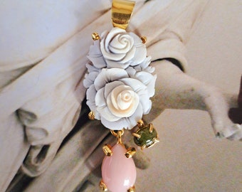 May include: A delicate gold pendant featuring two carved white roses with a pink teardrop-shaped gemstone and two green gemstones hanging below.