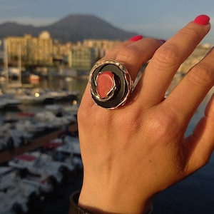 May include: A gold ring featuring a black and coral stone. The ring is worn on a person's finger.