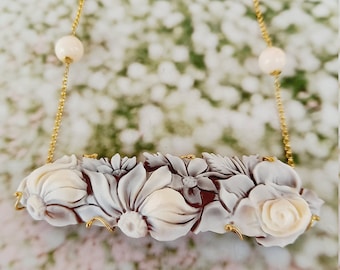 May include: A gold chain necklace with white shell flower carvings and white beads. The necklace is on a white background.
