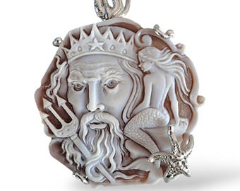 May include: A white and brown shell cameo pendant featuring a detailed carving of Poseidon, the Greek god of the sea, with a trident and a mermaid. The pendant is made of shell and silver.