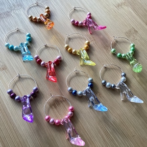 May include: Ten glass wine glass charms with clear glass shoe charms. Each charm has a different color of beads and a different colored shoe charm.
