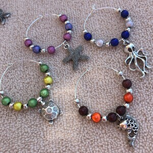 May include: Four silver wine glass charms with colorful beads and sea-themed charms. The charms include a starfish, an octopus, a turtle, and a fish.