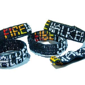 May include: Five beaded bracelets in black, white, yellow, orange, and red. The bracelets display the words "FIRE" and "WALKER" in a pixelated style. The bracelets are on a white background.