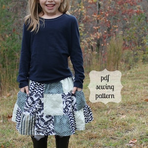 Könnte beinhalten: Ein junges Mädchen trägt ein marineblaues Langarmshirt und einen Patchworkrock mit Blumenmuster. Der Rock hat Taschen an den Seiten. Das Mädchen steht in einem grasbewachsenen Bereich mit Bäumen im Hintergrund. Der Text "pdf sewing pattern" steht auf einem weißen Etikett.