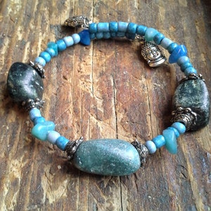May include: A blue and silver bracelet with a Buddha charm and green stone beads.