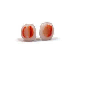 May include: A pair of white glass earrings with red and orange accents. The earrings are oval shaped and have a translucent appearance.