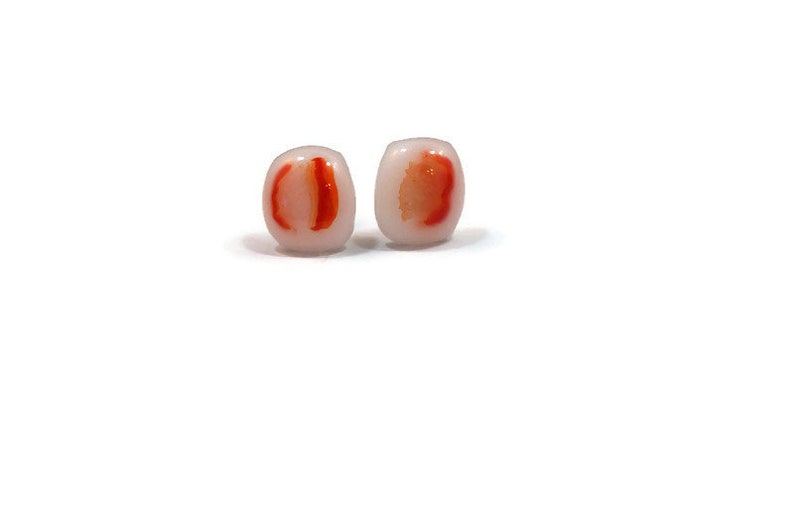 May include: A pair of white glass earrings with red and orange accents. The earrings are oval shaped and have a translucent appearance.