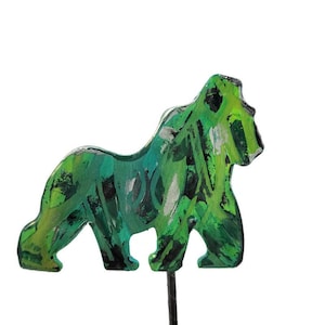 May include: A painted gorilla figurine in shades of green, black, and silver. The gorilla is standing on a dark metal rod, with a white background. The figurine has a textured, artistic appearance.