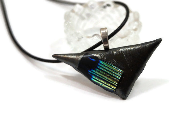 May include: A black pendant necklace with a triangular, textured pendant. The pendant has a silver bail and a section of iridescent blue and green glass. The necklace cord is black.