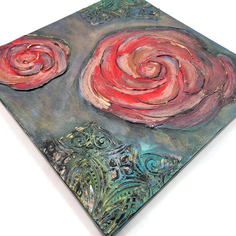 May include: Square canvas art featuring two raised red rose designs with gold accents. The background is a textured teal and gray with ornate green corner details. A unique piece of floral wall decor.