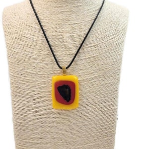 May include: A yellow, red, and black glass pendant necklace with a black cord. The pendant is rectangular and has a gold bail.