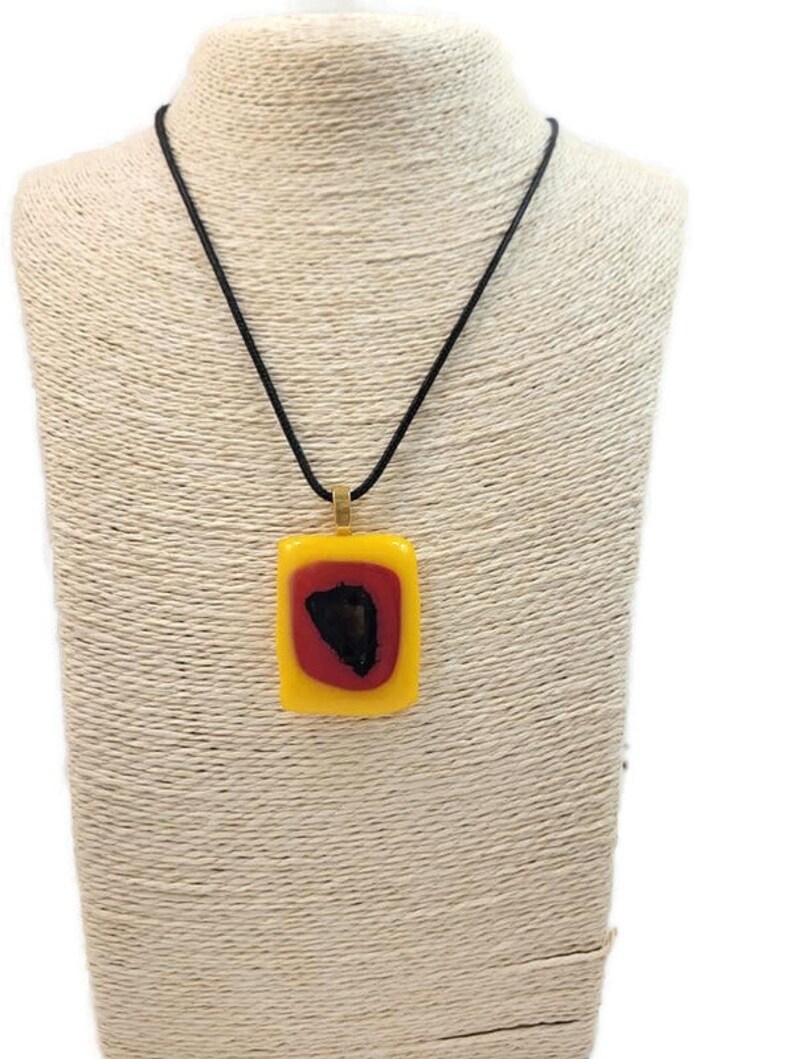 May include: A yellow, red, and black glass pendant necklace with a black cord. The pendant is rectangular and has a gold bail.