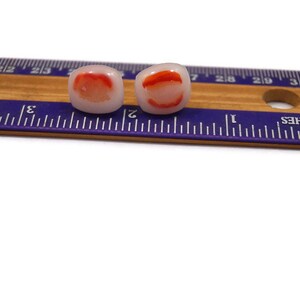 May include: Two white and red glass beads with a red swirl design. The beads are approximately 1/2 inch in diameter and are shown next to a ruler.