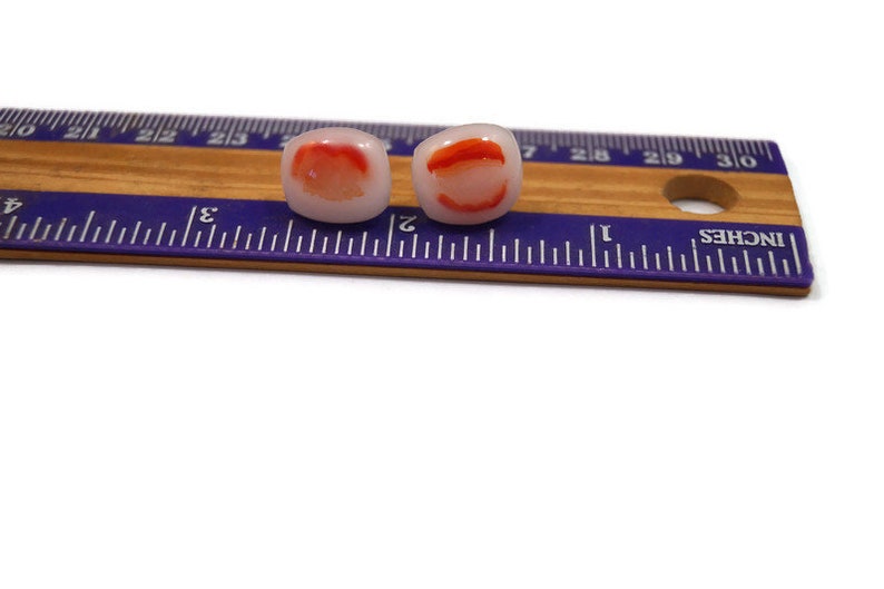 May include: Two white and red glass beads with a red swirl design. The beads are approximately 1/2 inch in diameter and are shown next to a ruler.