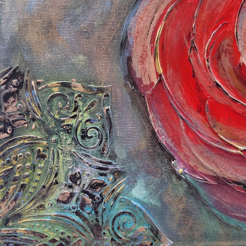 May include: Close-up of an abstract painting featuring a vibrant red rose and a decorative, ornate green and bronze element. The artwork has a textured appearance with visible brushstrokes, set against a muted, blended background.