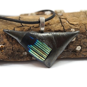 May include: A triangular pendant necklace with a black finish and a section of iridescent blue and green glass. The pendant is suspended from a black cord and has a silver-colored bail. The necklace is displayed on a piece of driftwood.