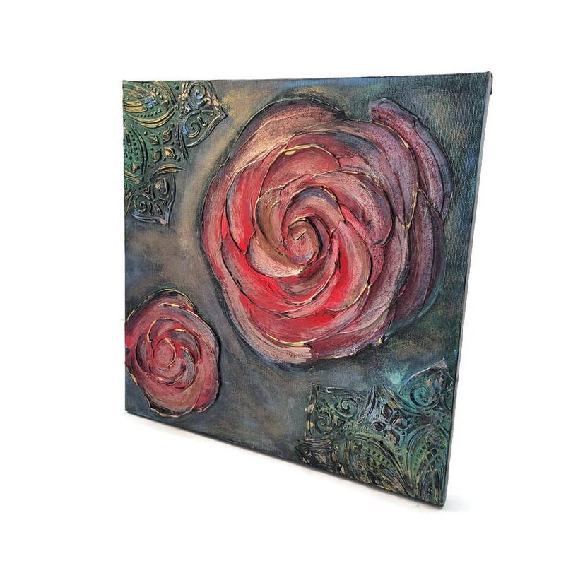 May include: Square canvas art featuring a textured, raised relief of a large red rose with gold accents, and a smaller rose. The background is a dark gray with green and gold decorative corner elements.