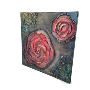May include: Square canvas art featuring two textured red roses with gold accents against a gray and blue background. Decorative green and gold corner accents add detail. The artwork is displayed at an angle.
