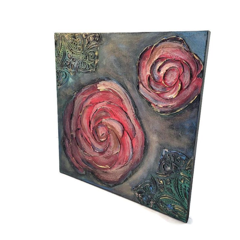 May include: Square canvas art featuring two textured red roses with gold accents against a gray and blue background. Decorative green and gold corner accents add detail. The artwork is displayed at an angle.