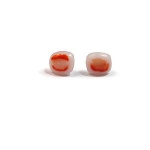 May include: A pair of small square earrings with a white background and a red and orange design.