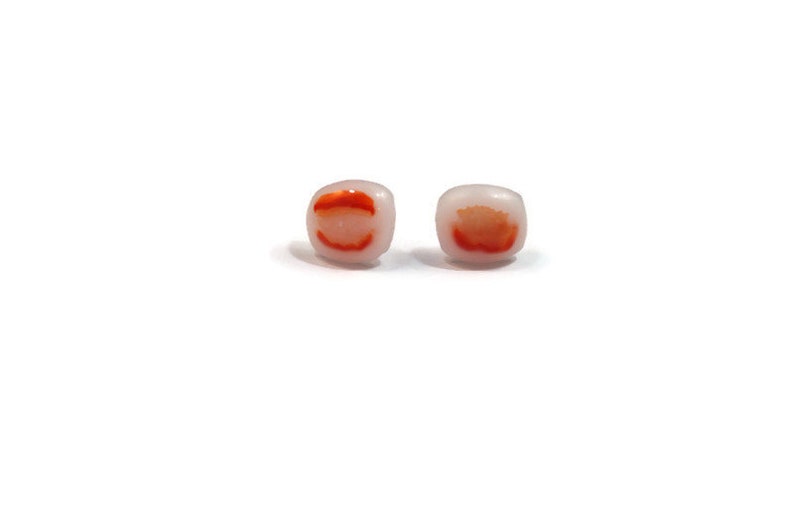 May include: A pair of small square earrings with a white background and a red and orange design.