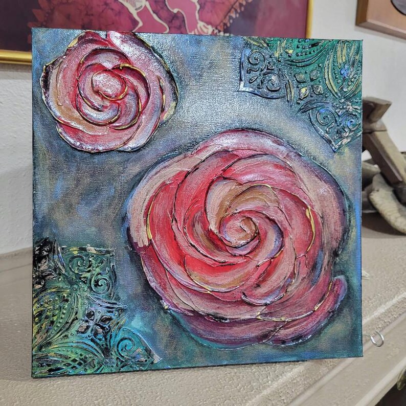 May include: Square canvas art featuring textured, raised roses in shades of red, pink, and gold. The background is a blend of blue and gray with decorative teal accents. The artwork has a three-dimensional effect.
