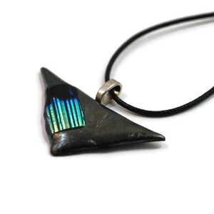 May include: A triangular pendant necklace with a black cord. The pendant is dark gray with a section of iridescent blue and green glass. The necklace has a silver-colored bail.