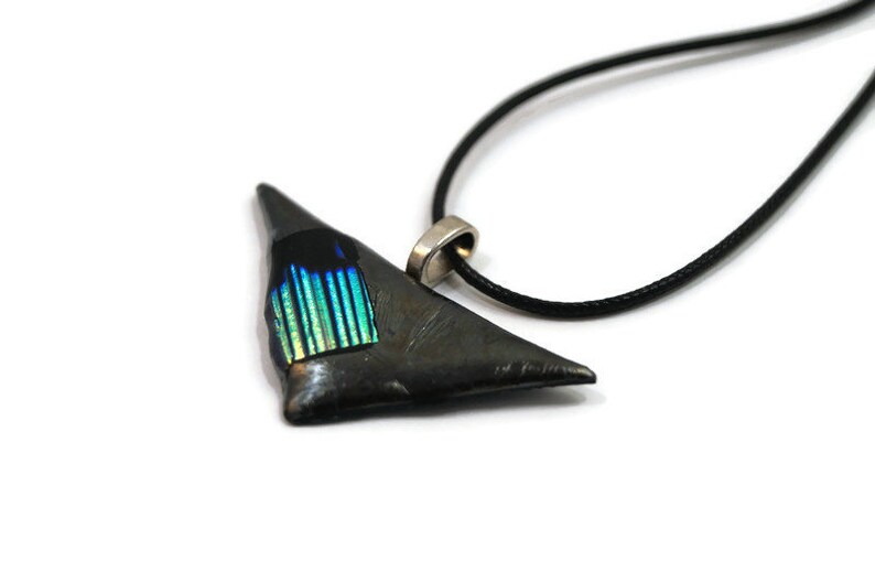 May include: A triangular pendant necklace with a black cord. The pendant is dark gray with a section of iridescent blue and green glass. The necklace has a silver-colored bail.