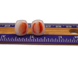 May include: A pair of white and red glass earrings. The earrings are shaped like a slice of fruit, with a red center and white edges. The earrings are about 1 inch long.