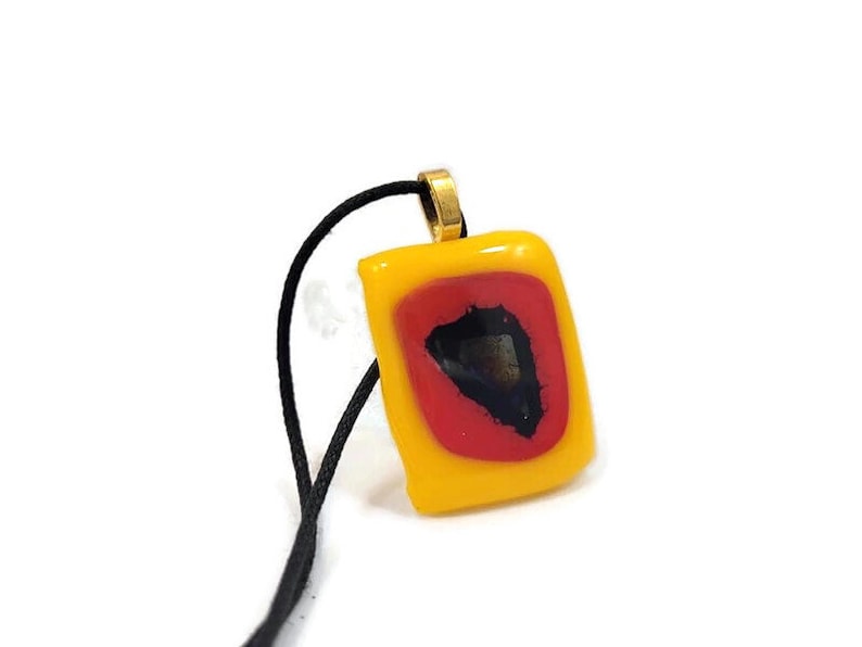 May include: A yellow glass pendant with a red and black design, hanging from a black cord.