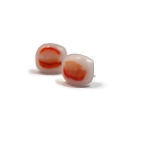 May include: A pair of small, square earrings with a white background and red and orange swirls.