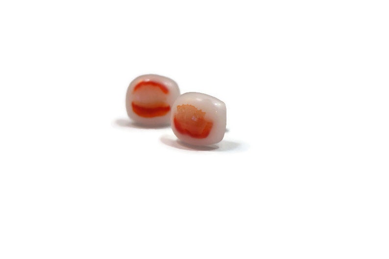 May include: A pair of small, square earrings with a white background and red and orange swirls.